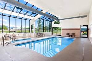 A modern indoor swimming pool with large windows, a clear view of the outdoors, and a simple seating area.