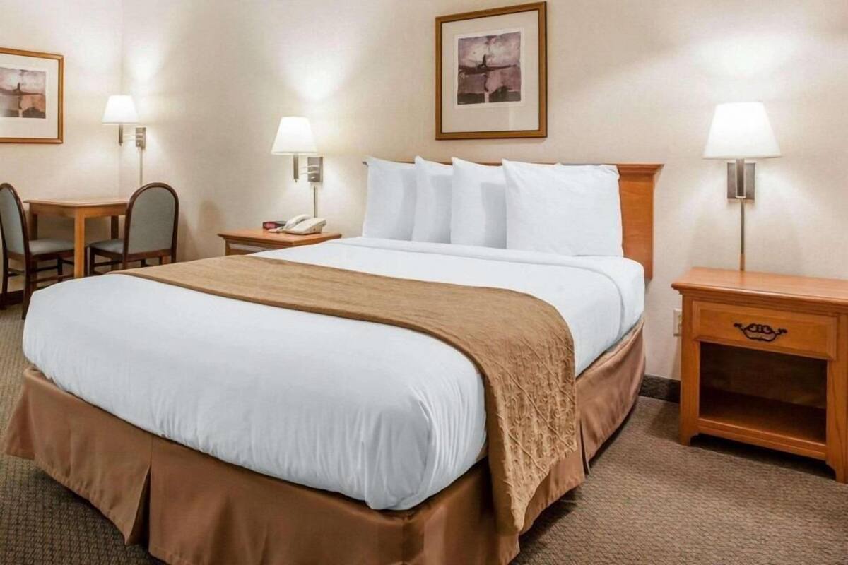 A hotel room with a large bed, two bedside tables, a desk with a chair, and a lamp.