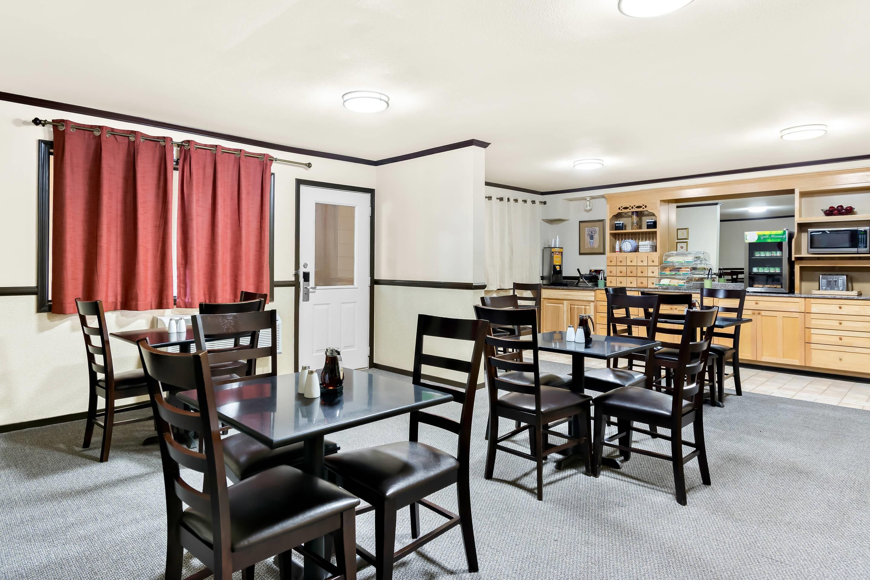 A dining area with a table and chairs, a kitchen area with a microwave and refrigerator, and a door with a red curtain.