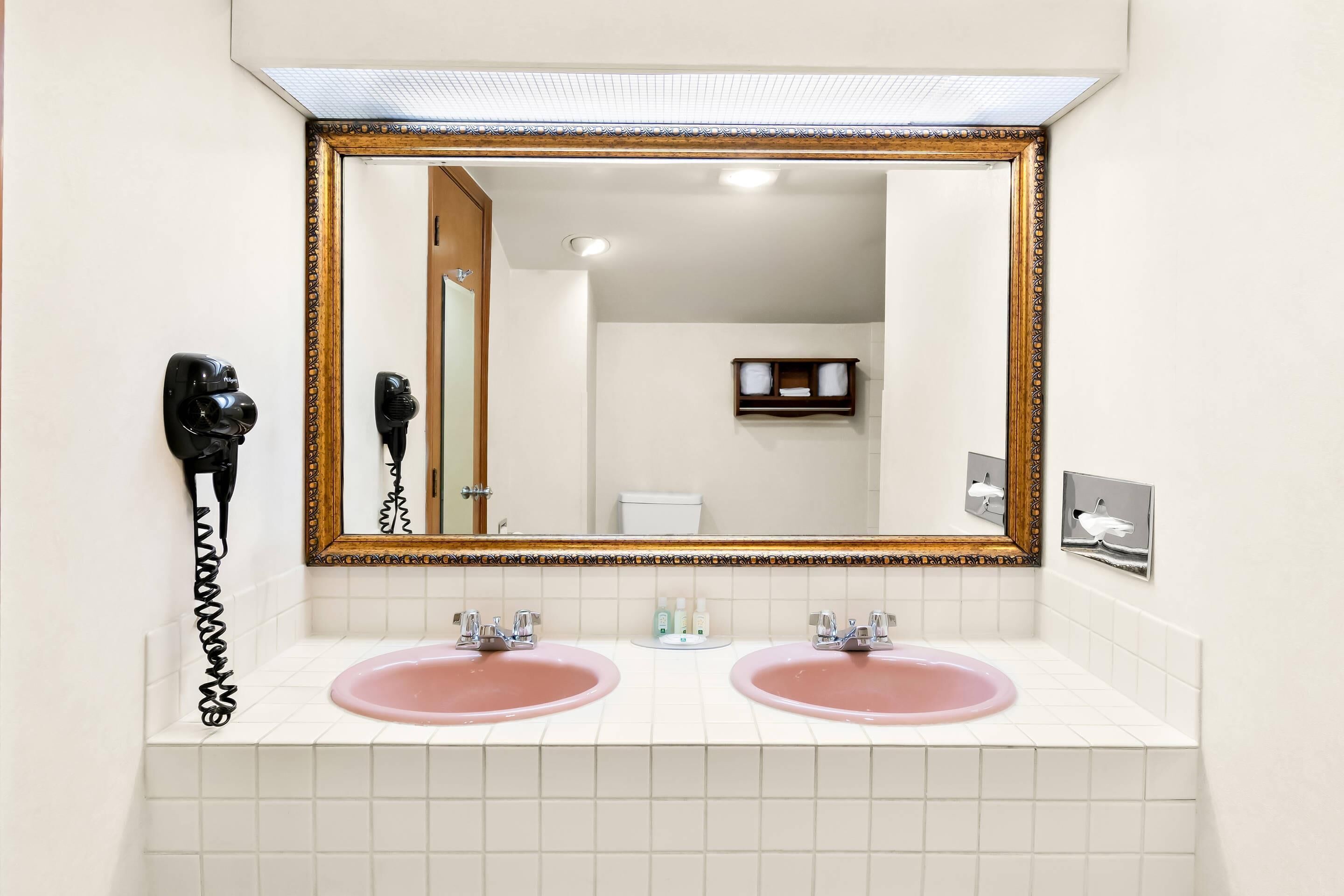 A bathroom with two sinks, a large mirror, and a hairdryer on the wall.