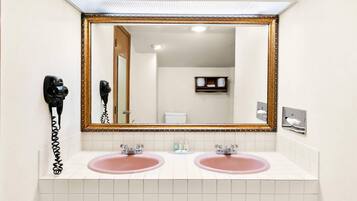 A bathroom with two sinks, a large mirror, and a hairdryer on the wall.