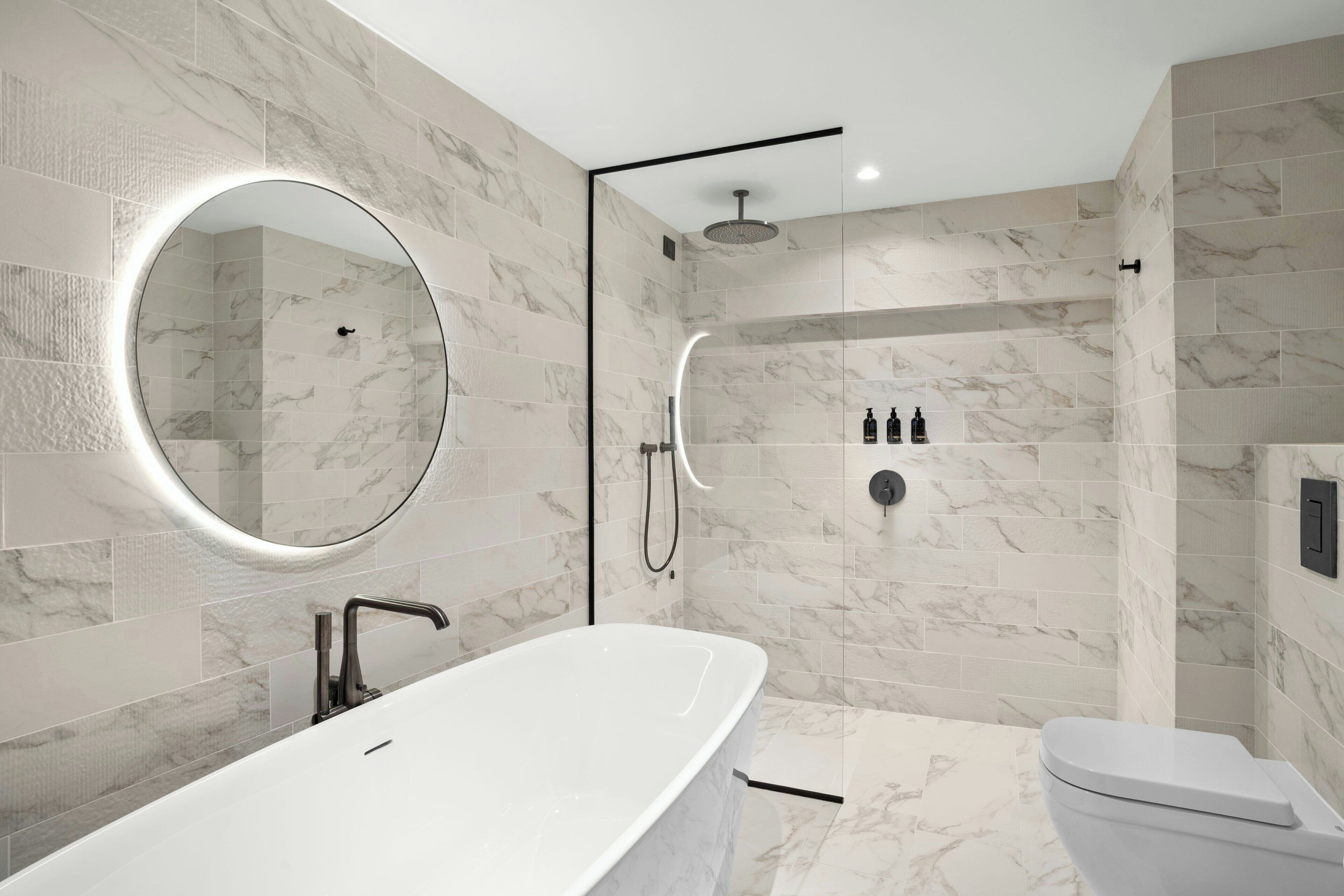 Un baño moderno con una bañera independiente, un espejo redondo, una ducha con cerramiento de vidrio y un inodoro.