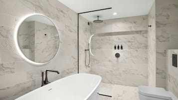 Un baño moderno con una bañera independiente, un espejo redondo, una ducha con cerramiento de vidrio y un inodoro.
