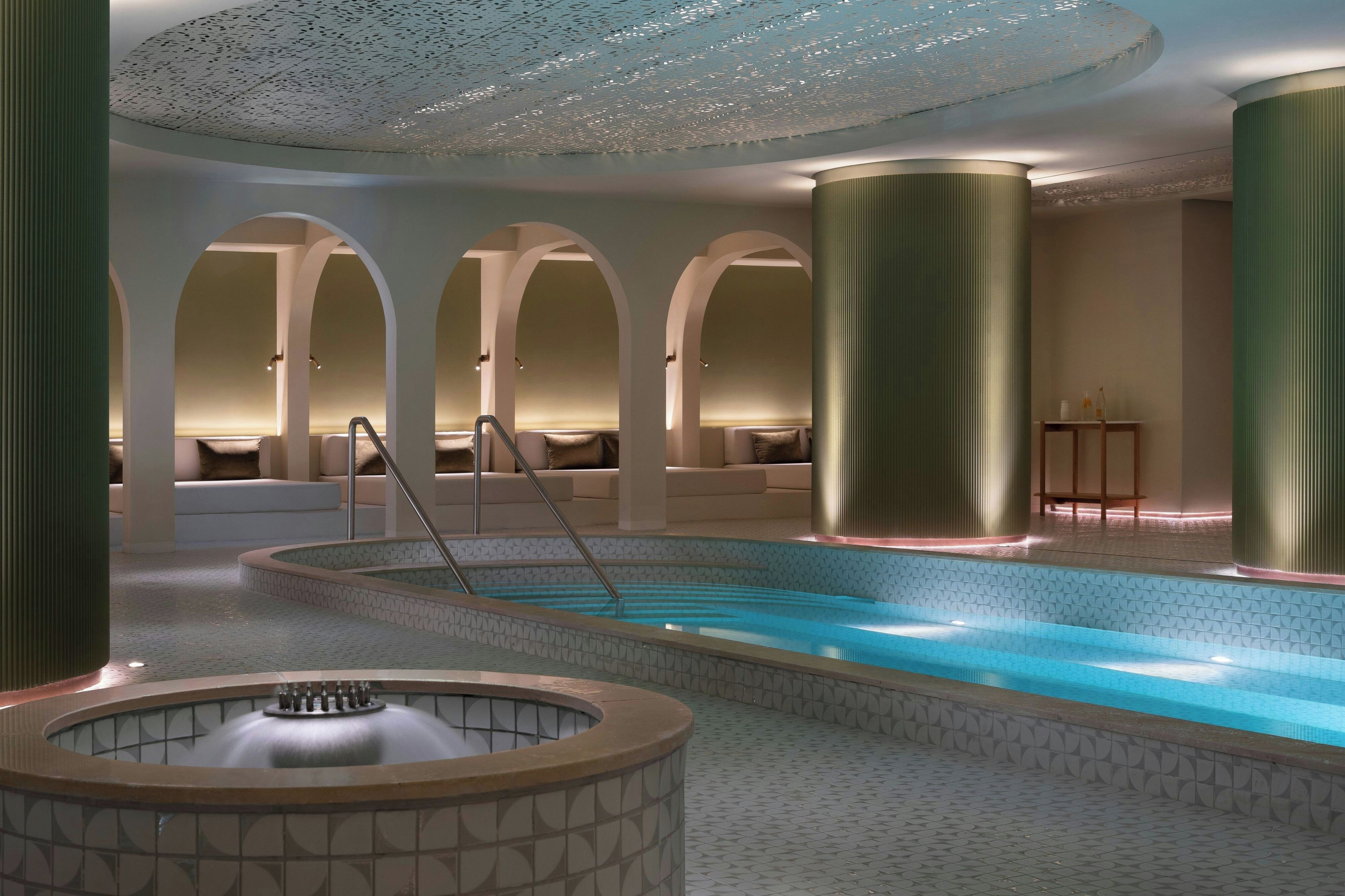 A modern indoor pool area with a central hot tub, seating areas, and a ceiling with a unique pattern.
