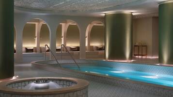 A modern indoor pool area with a central hot tub, seating areas, and a ceiling with a unique pattern.