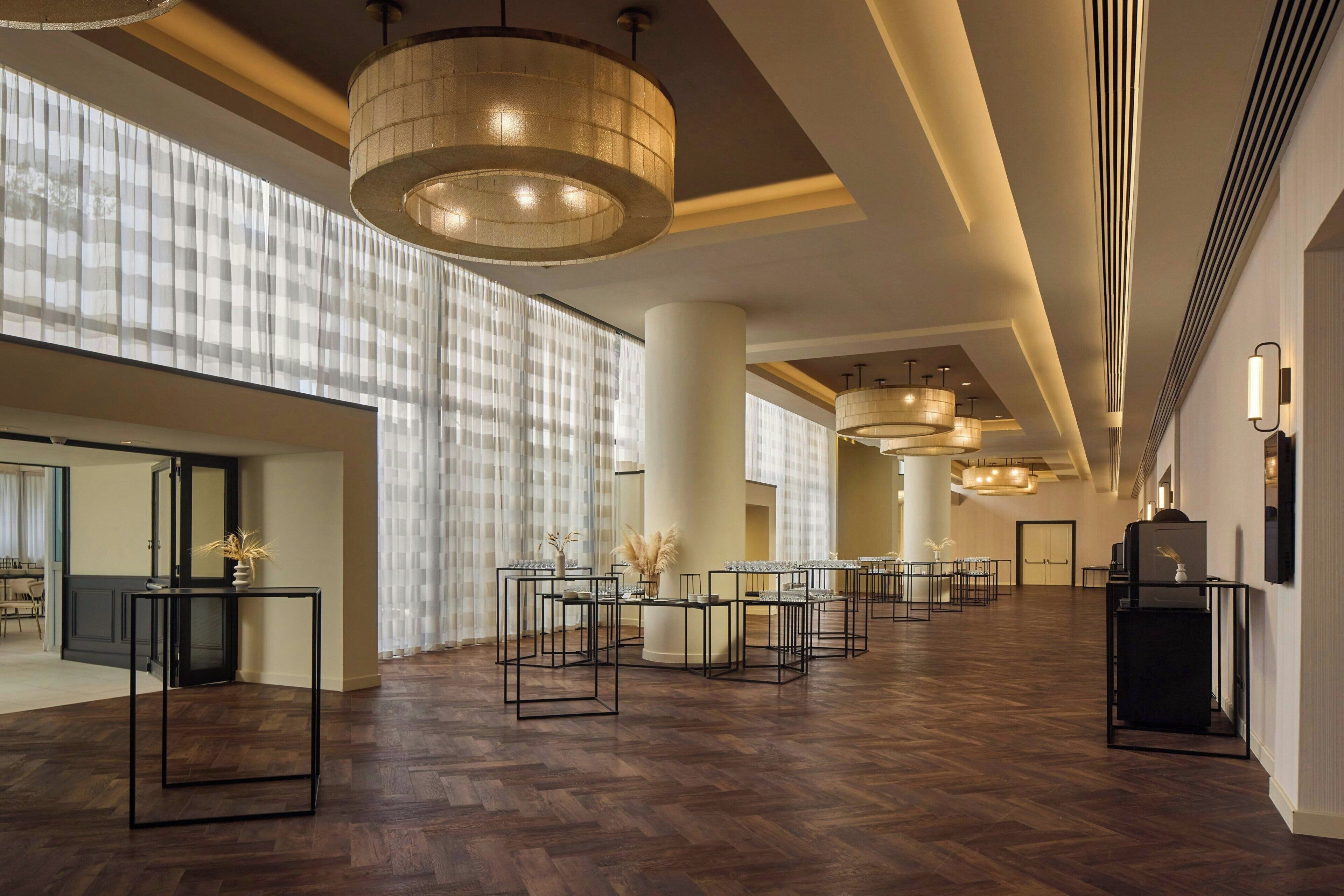 A spacious hotel lobby with high ceilings, large windows with sheer curtains, and multiple seating areas.