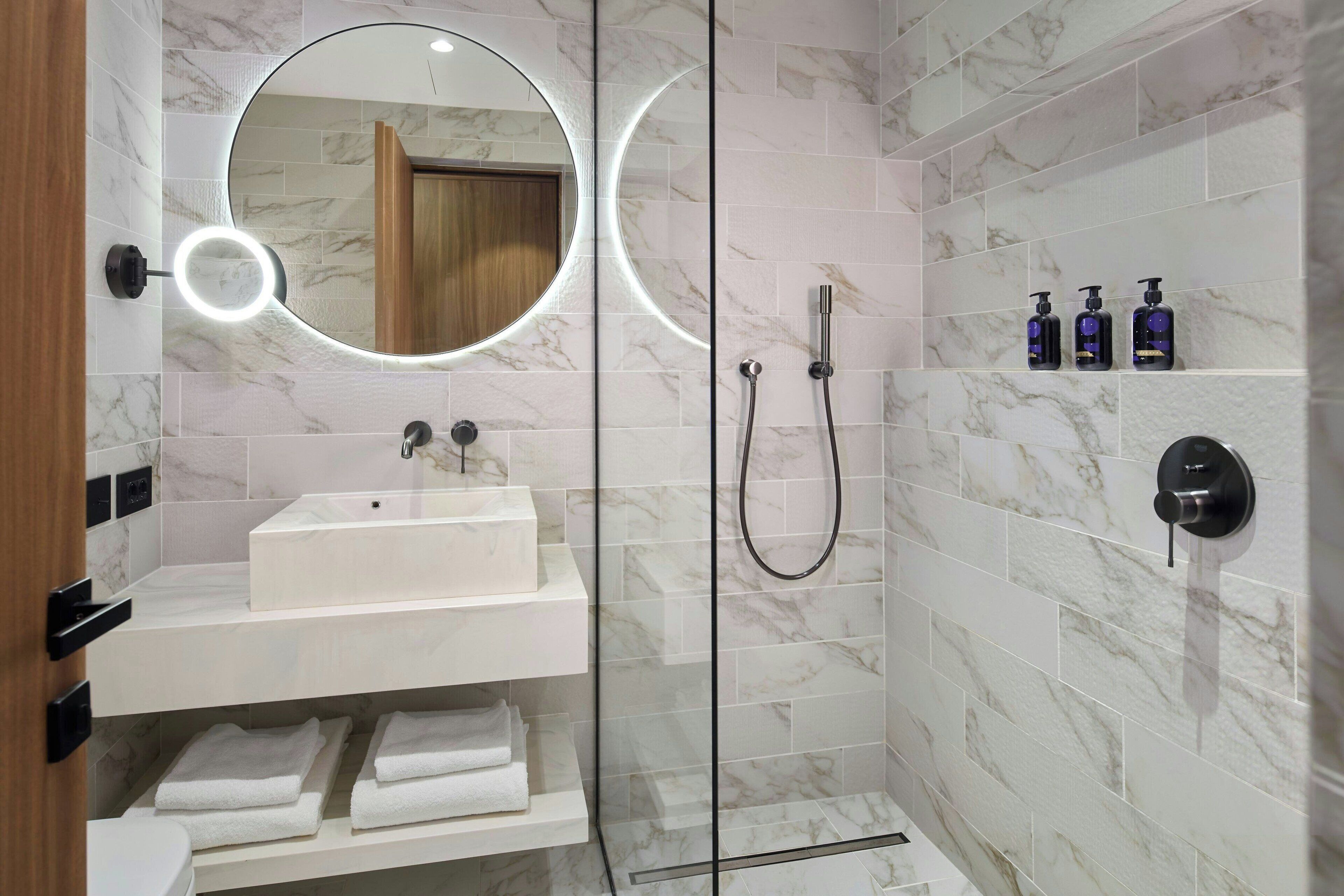A modern bathroom with a white sink, a glass-enclosed shower, and a marble-tiled wall.