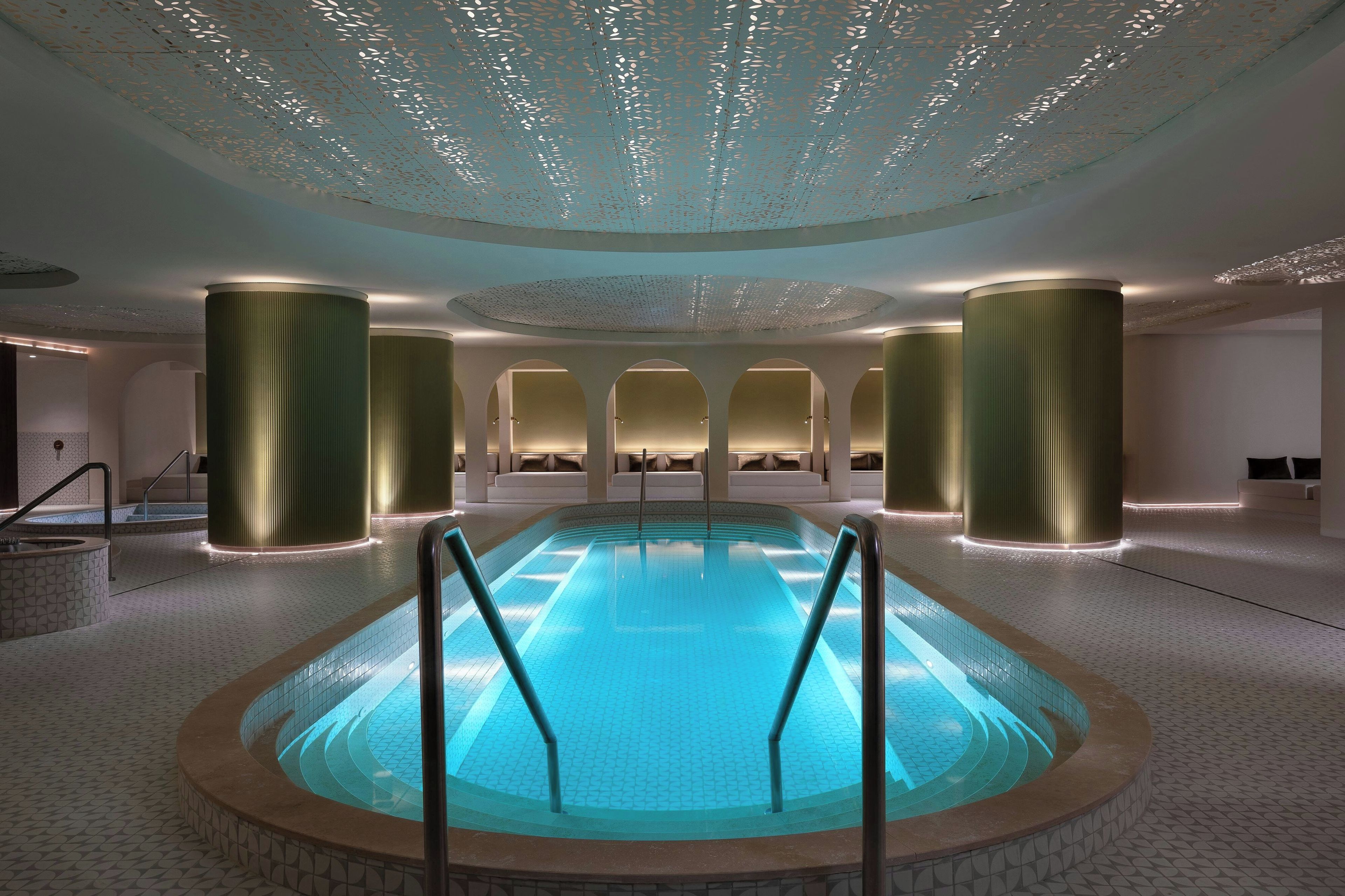 Une piscine intérieure moderne, avec une eau d’un bleu limpide, entourée d’un sol à motifs et éclairée par des luminaires encastrés.