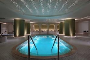 A modern indoor swimming pool with a clear blue water surface, surrounded by a patterned floor, and illuminated by recessed lighting. - Cardo Roma, Autograph Hotel (Rome)
