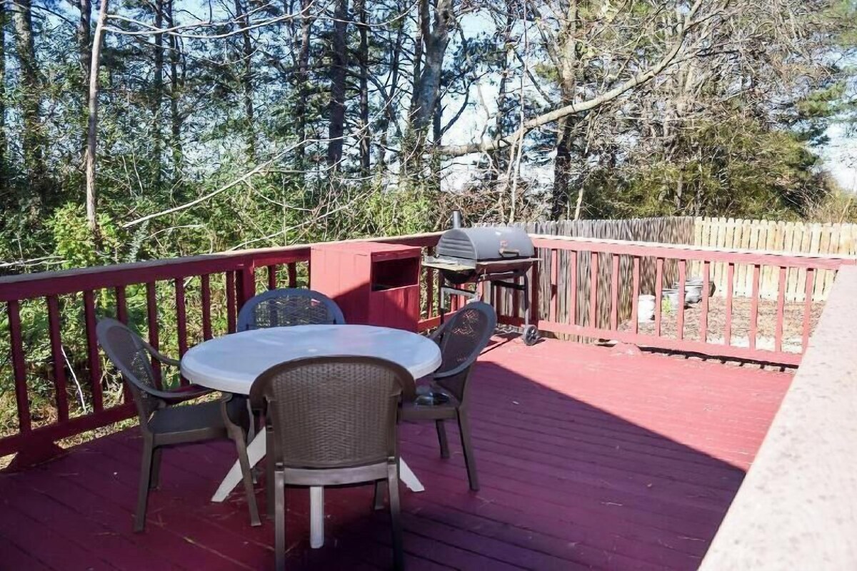 Une terrasse extérieure couverte, dotée d’une table ronde et de chaises, d’un barbecue et d’une clôture en bois.