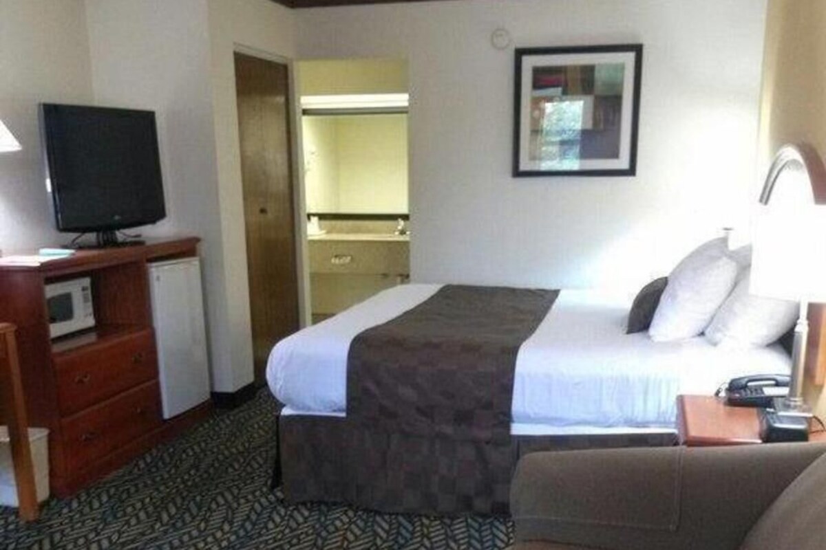 Une chambre d’hôtel équipée d’un lit, d’une télévision, d’un bureau avec un ordinateur et d’une salle de bain visible à travers une porte ouverte.