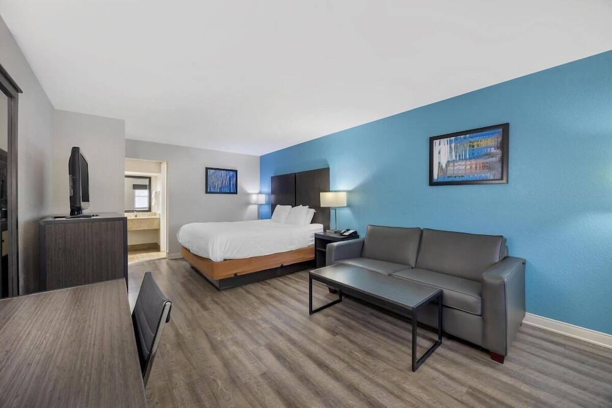 Quarto de hotel com cama, sofá, escrivaninha e televisão.