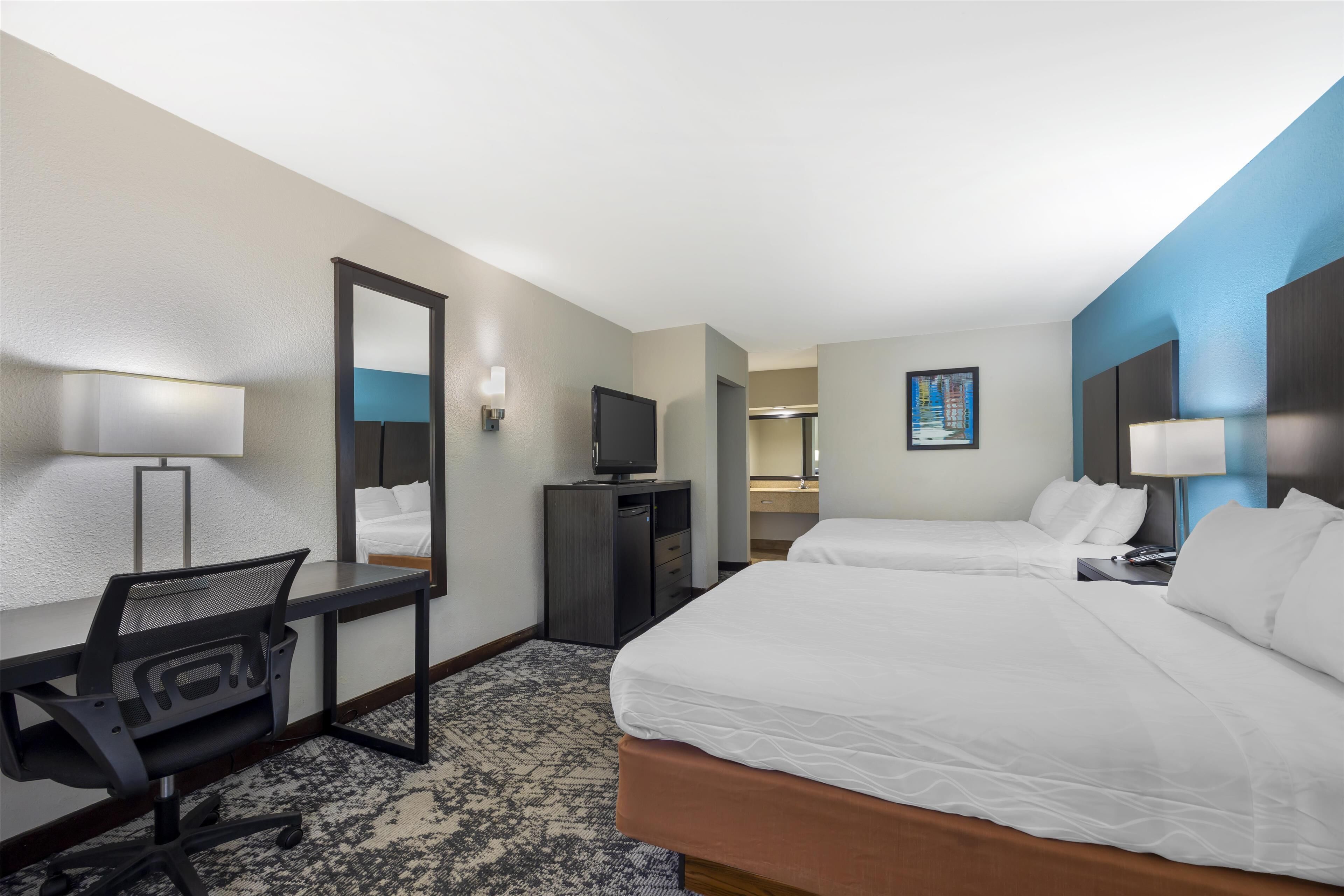 A hotel room with two beds, a desk with a chair, a television, and a mirror.