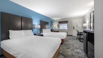 A hotel room with two beds, a desk, a chair, a TV, and a window.