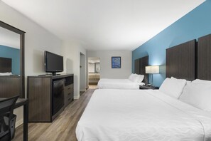 A hotel room with two beds, a desk with a television, a mirror, and a nightstand with a lamp.