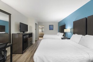 Una habitación de hotel con dos camas, un escritorio con televisor, un espejo y una mesita de noche con lámpara.