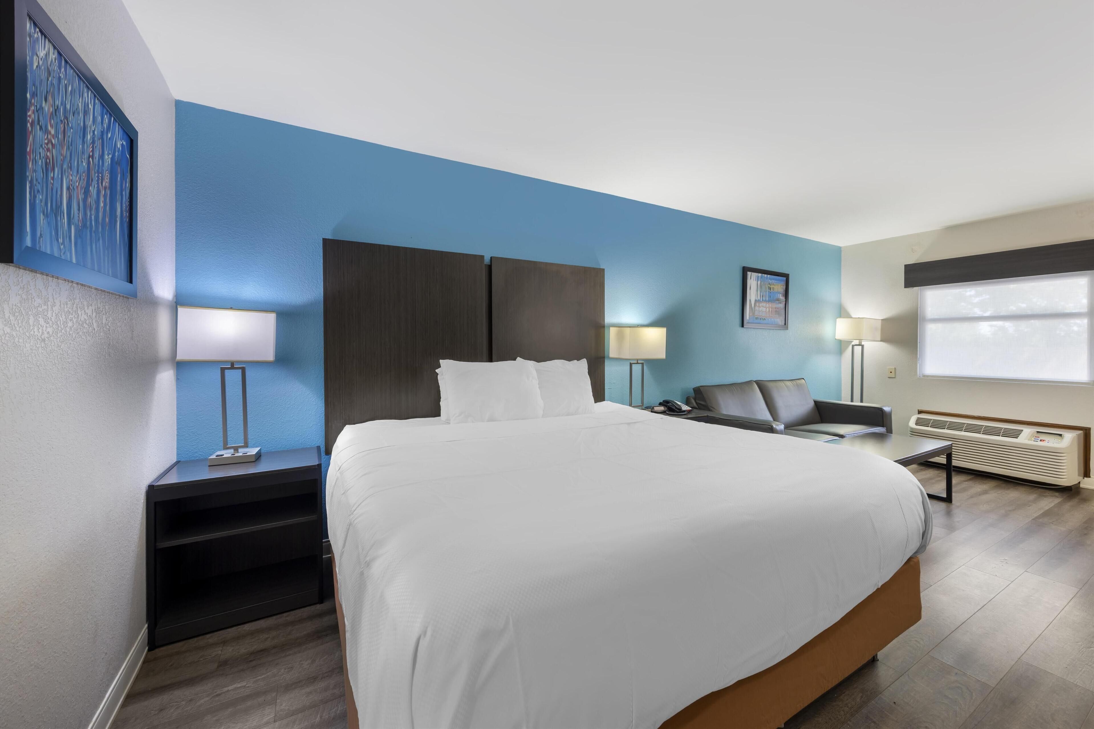 A hotel room with a large bed, a desk, a chair, a lamp, and a window.