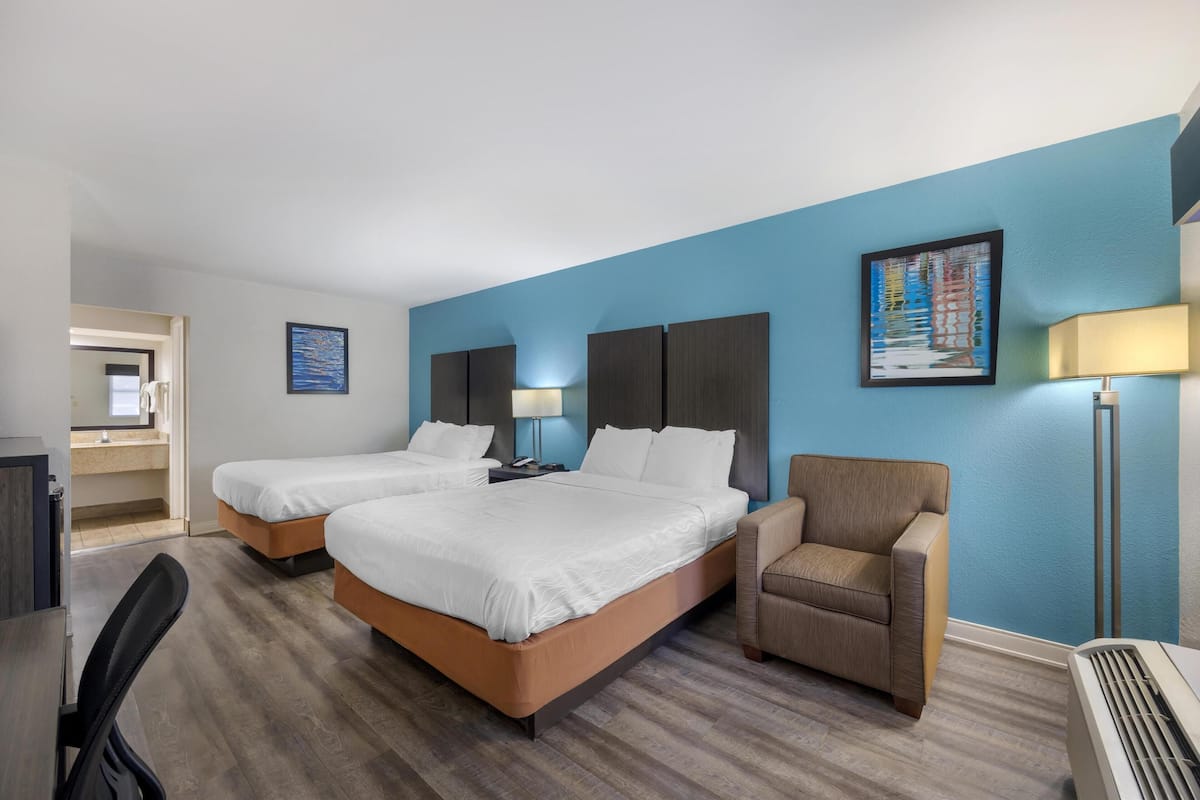 Quarto de hotel com duas camas, uma escrivaninha, uma cadeira e aquecedor.