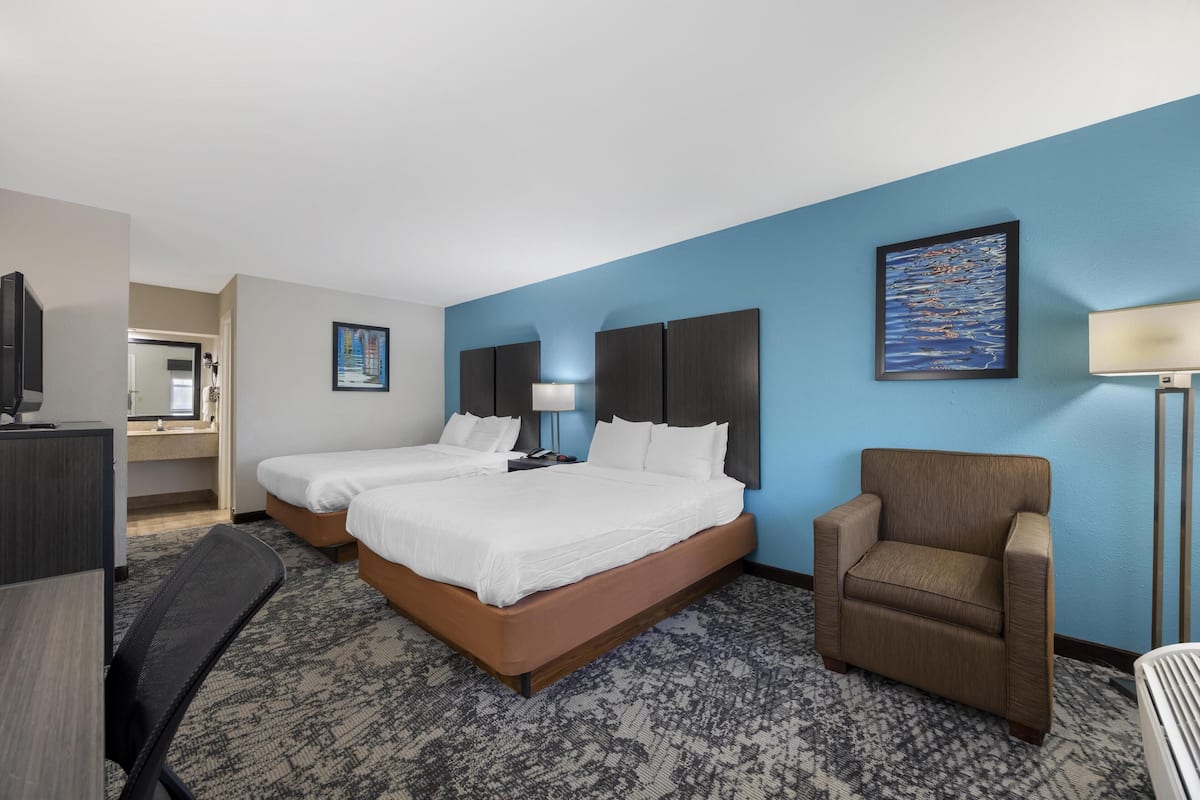 Quarto de hotel com duas camas, uma mesa, uma cadeira e uma televisão.