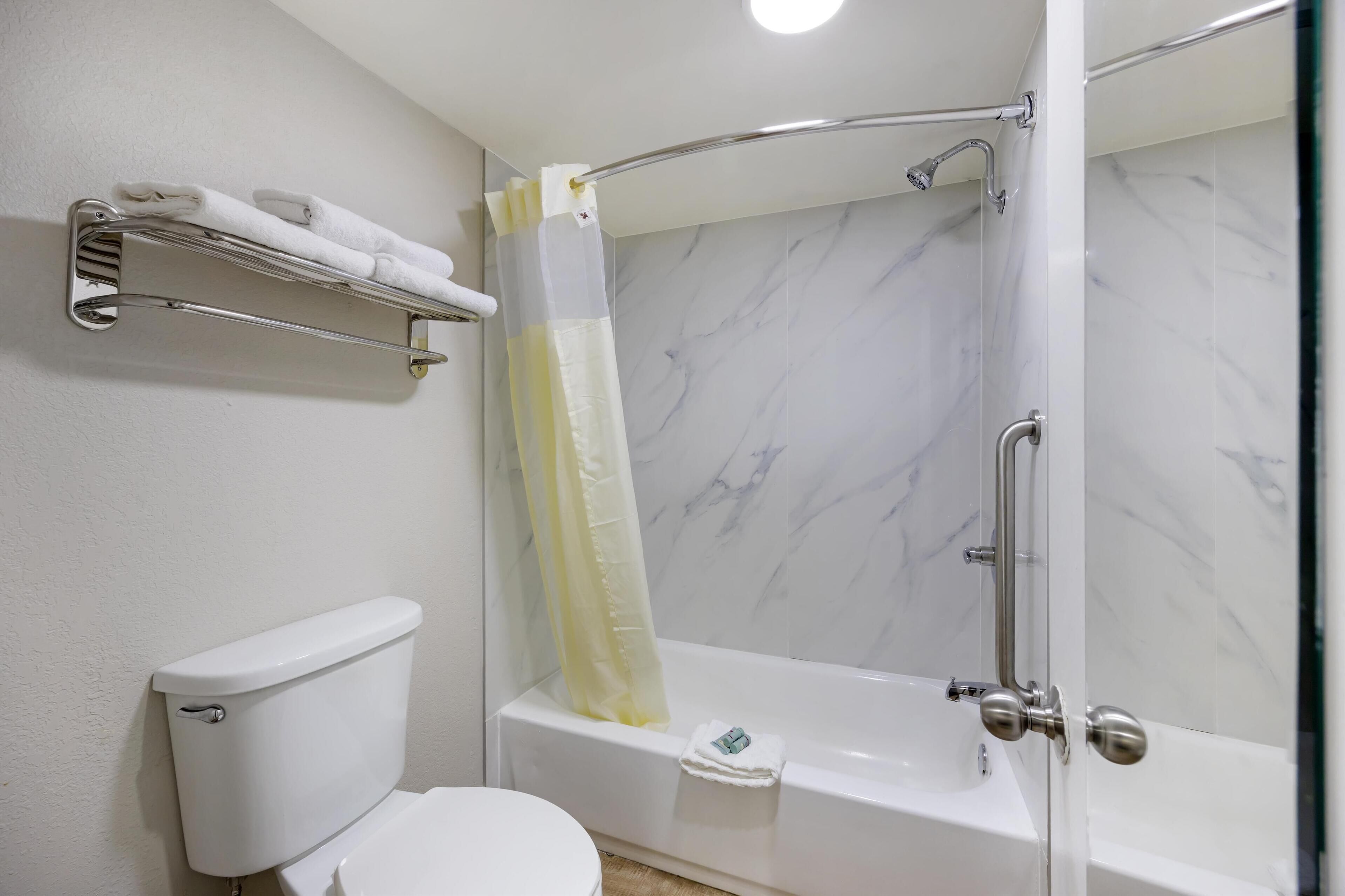 Un baño con inodoro, ducha con puerta de cristal y toallero con toallas dobladas.
