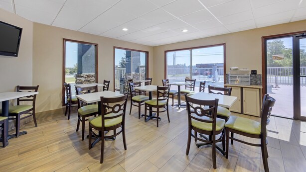 A dining area with wooden tables and chairs, large windows, and a flat-screen TV mounted on the wall. - Best Western Fairwinds Inn (Cullman)