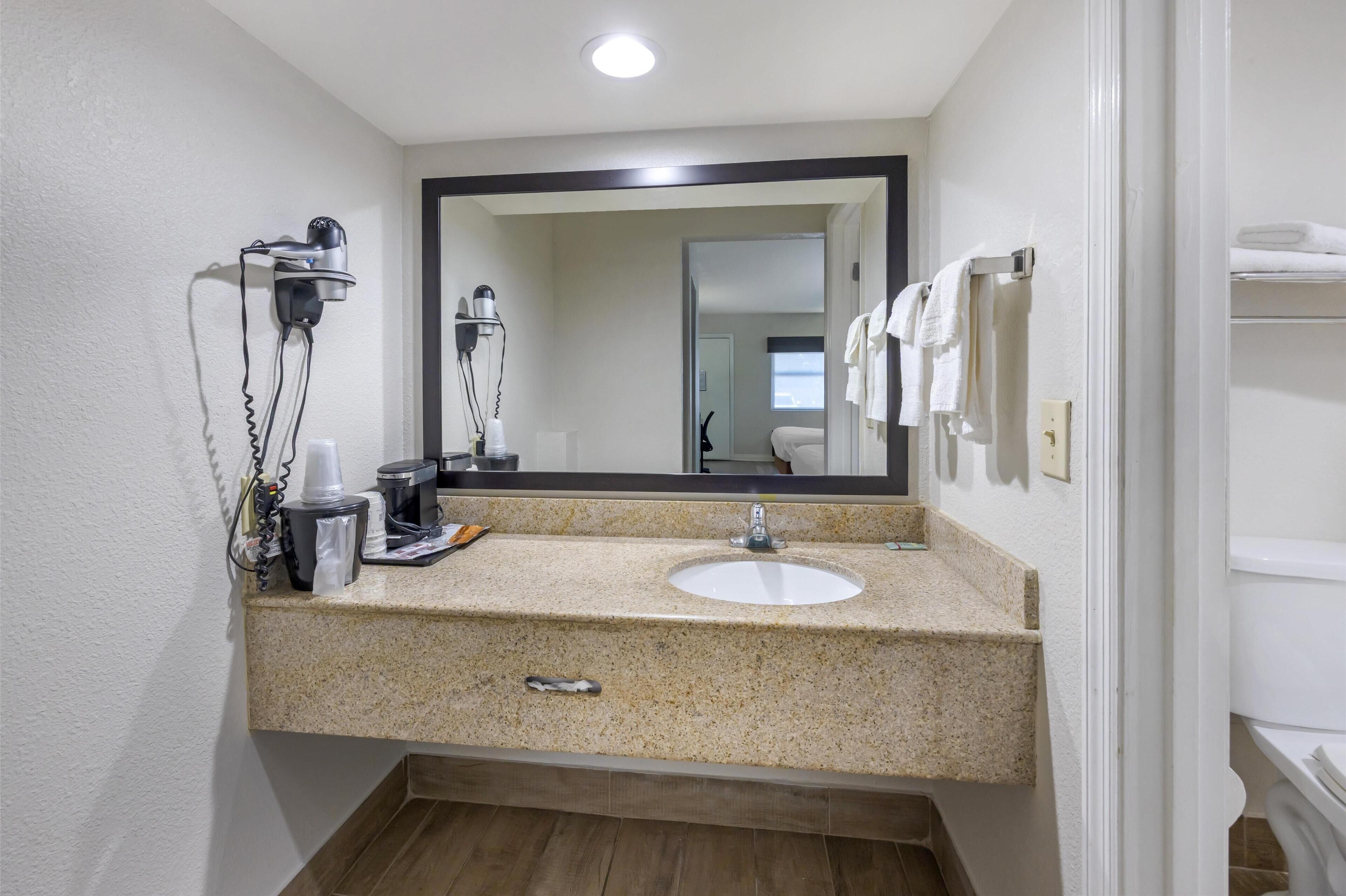 A bathroom with a granite countertop, a sink, a mirror, a hairdryer, and a towel rack.