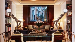 A well-lit living room with a large window, a sofa, a glass coffee table, and two bronze sculptures. - Hotel Lord Byron (Rome)
