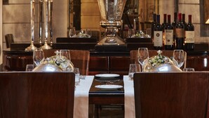 A formal dining room with a long table set for multiple guests, a large vase with flowers, tall candles, and wine bottles. - Hotel Lord Byron (Rome)