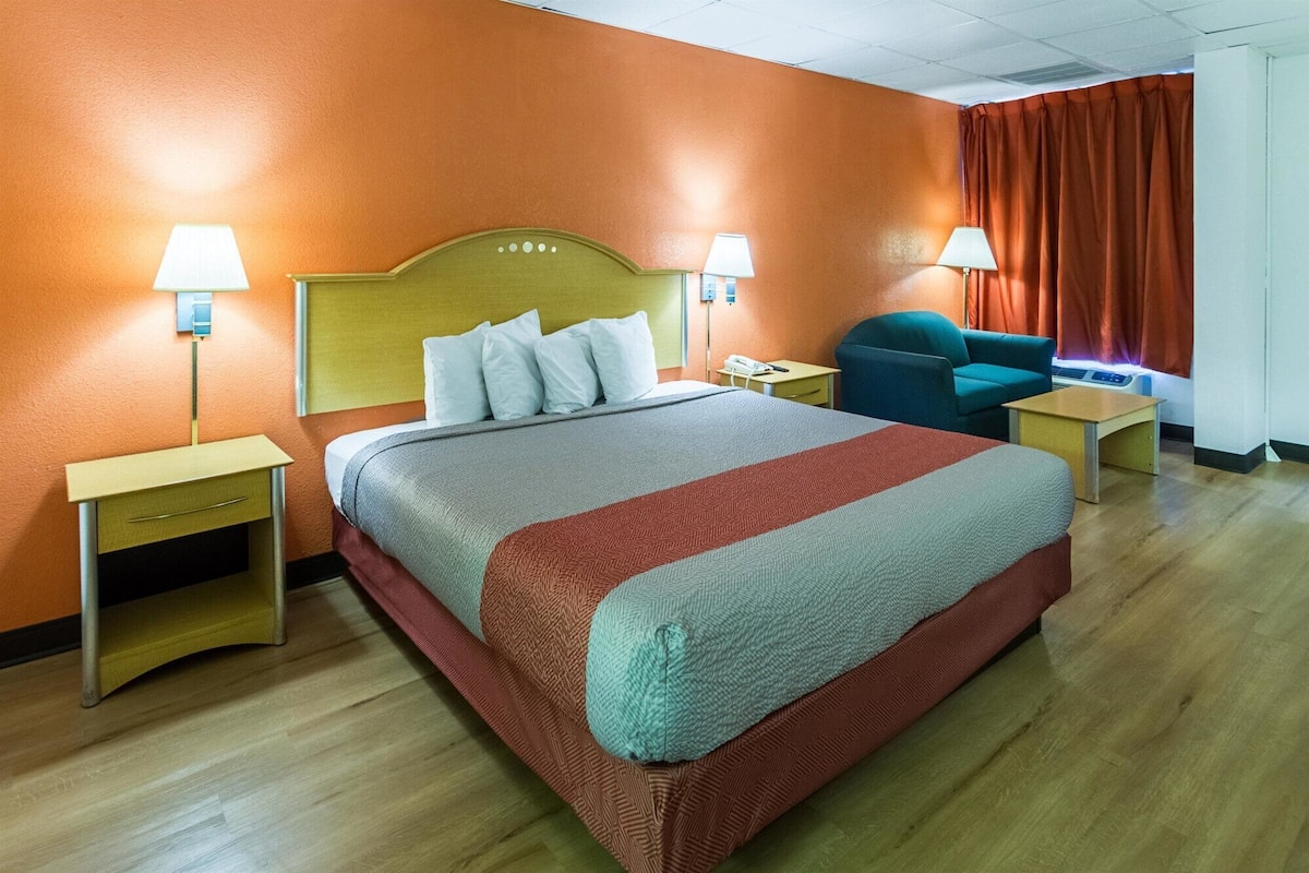 A hotel room with a bed, two bedside tables, a chair, a desk, and a window with curtains.