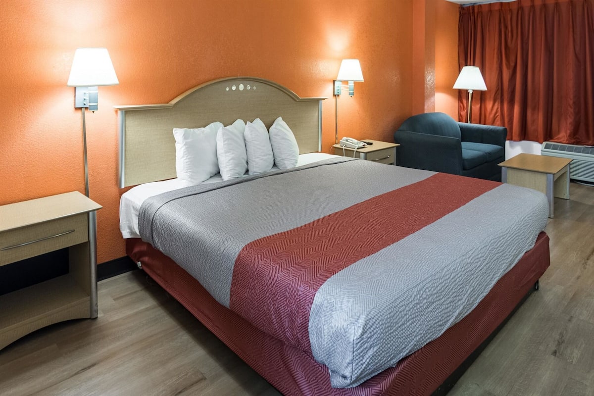 A hotel room with a bed, two bedside tables, a chair, a desk, and a telephone.