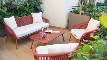 A red wicker sofa with white cushions, a matching red armchair, and a small table with a glass of wine and a book.