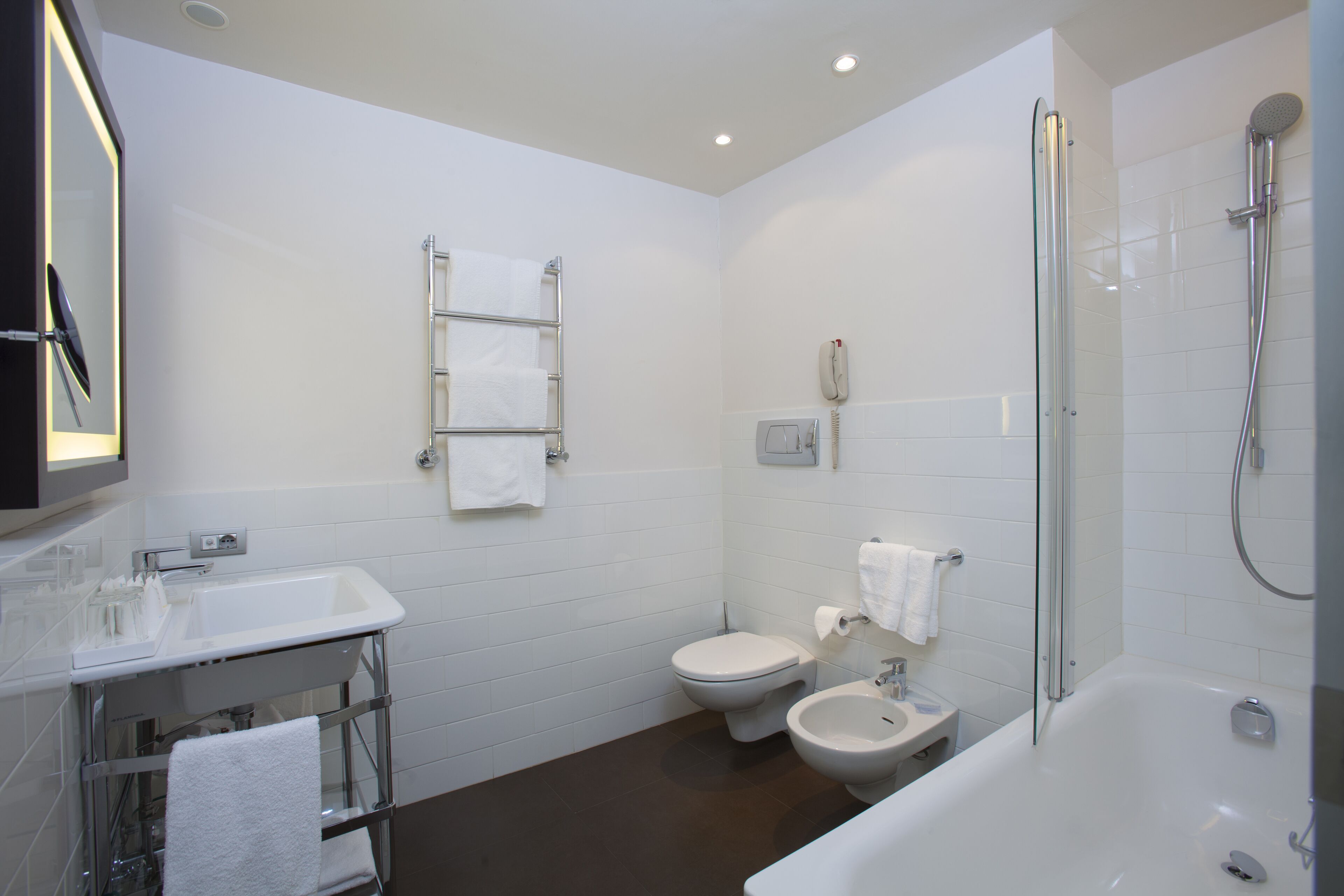A modern bathroom with a glass shower enclosure, a white sink, a toilet, and a bidet.