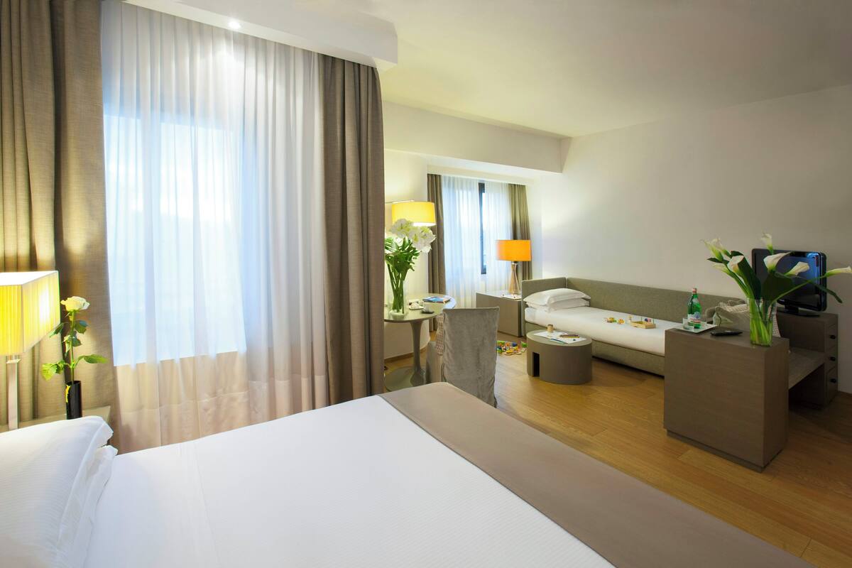 A hotel room with a large bed, a sofa, a coffee table, and a desk with a lamp and flowers.