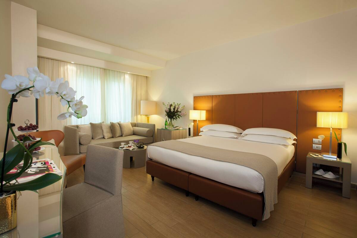 A hotel room with a large bed, a sofa, a coffee table, and a desk with a lamp.