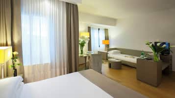 Ein Hotelzimmer mit einem großen Bett, einem Sofa, einem Couchtisch und einem Schreibtisch mit Lampe und Blumen.