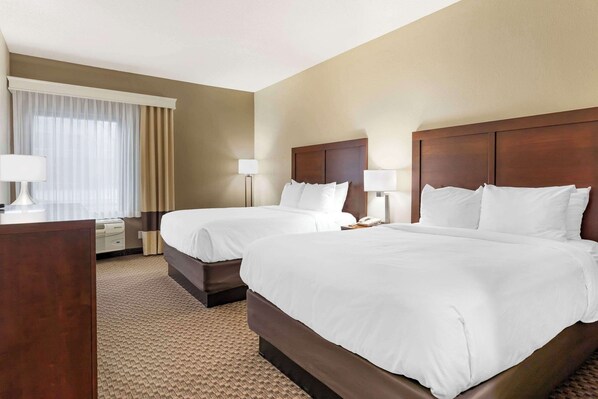A hotel room with two beds, a desk, and a window with curtains.