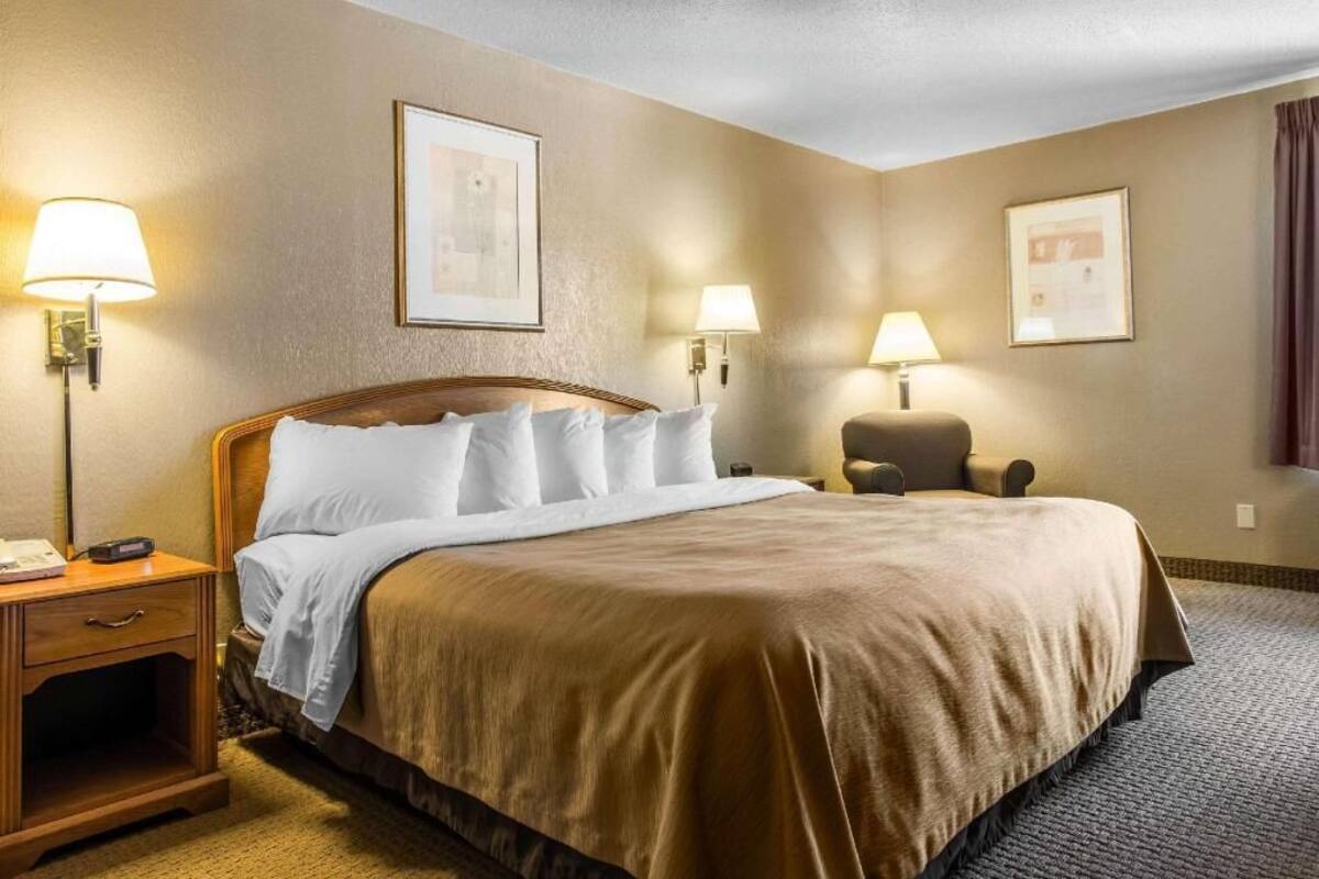 Una habitación de hotel con cama, lámparas de noche, una silla y mesita de noche.