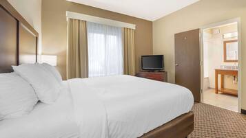 Habitación de hotel con una cama grande, televisión, escritorio y baño visible a través de una puerta abierta.