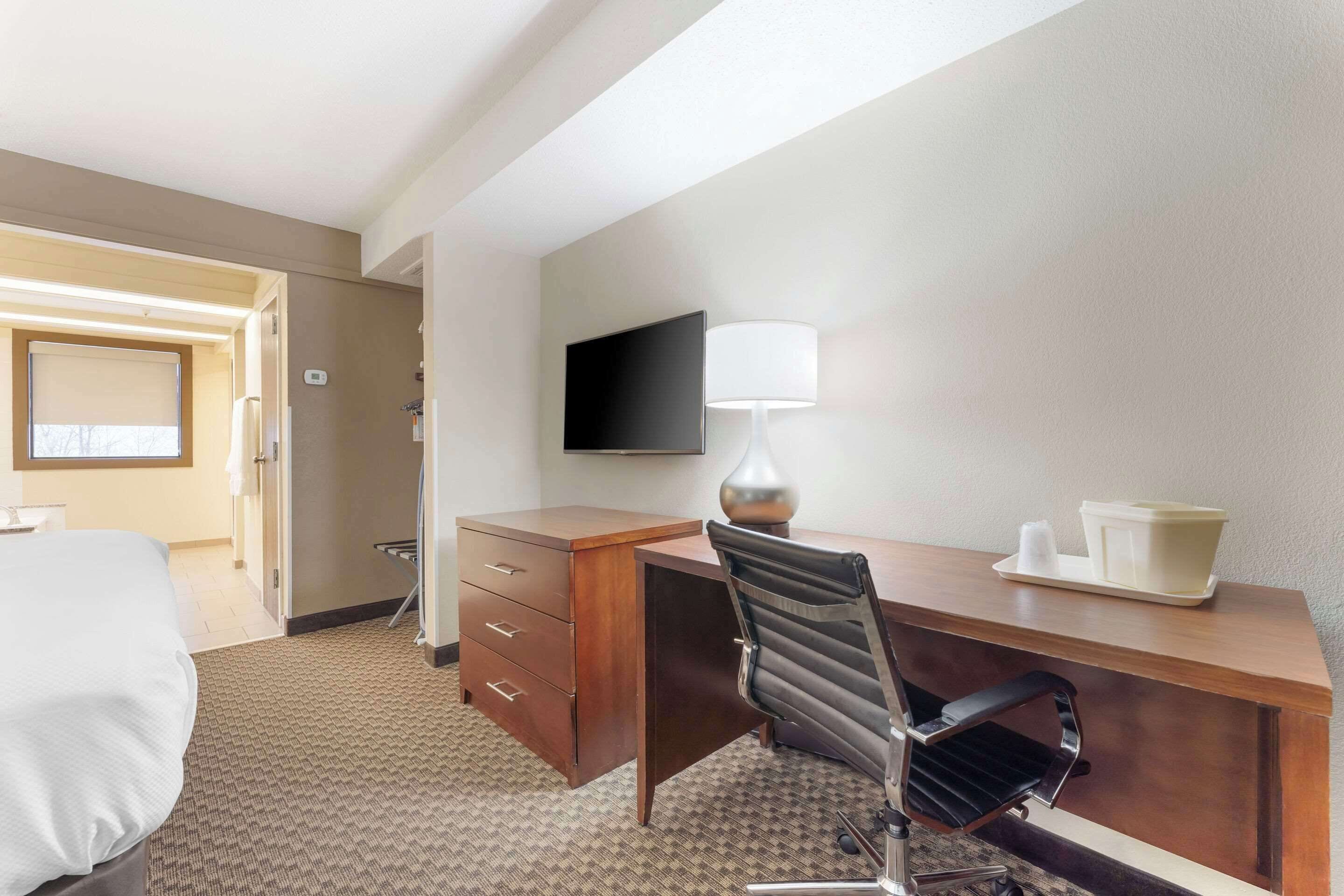 Een hotelkamer met een bed, een bureau met stoel, een aan de muur bevestigde televisie en een lamp op het bureau.