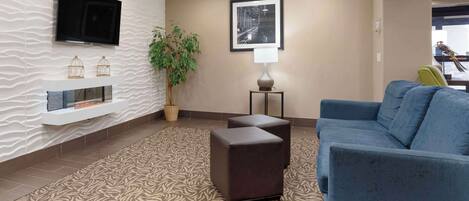 A modern lobby with a blue sofa, a patterned rug, a flat-screen TV, a framed picture, and a potted plant.