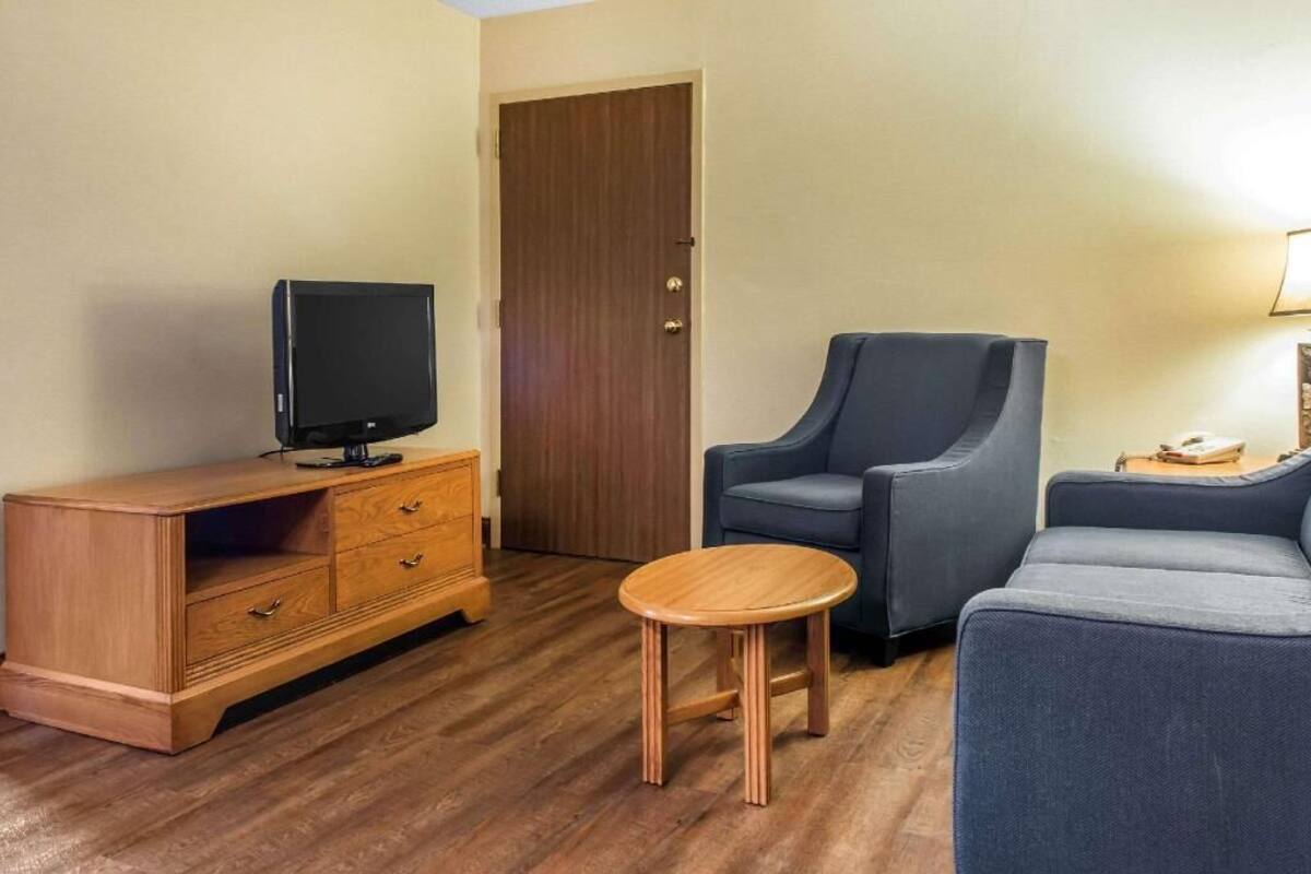 Una habitación con un armario de madera, un televisor, un sillón azul, un sofá y una pequeña mesa de madera.