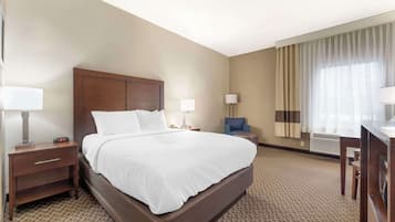 Ein Hotelzimmer mit einem großen Bett, einem Nachttisch mit Lampe, einem Schreibtisch mit Stuhl und einem Fenster mit Vorhängen.