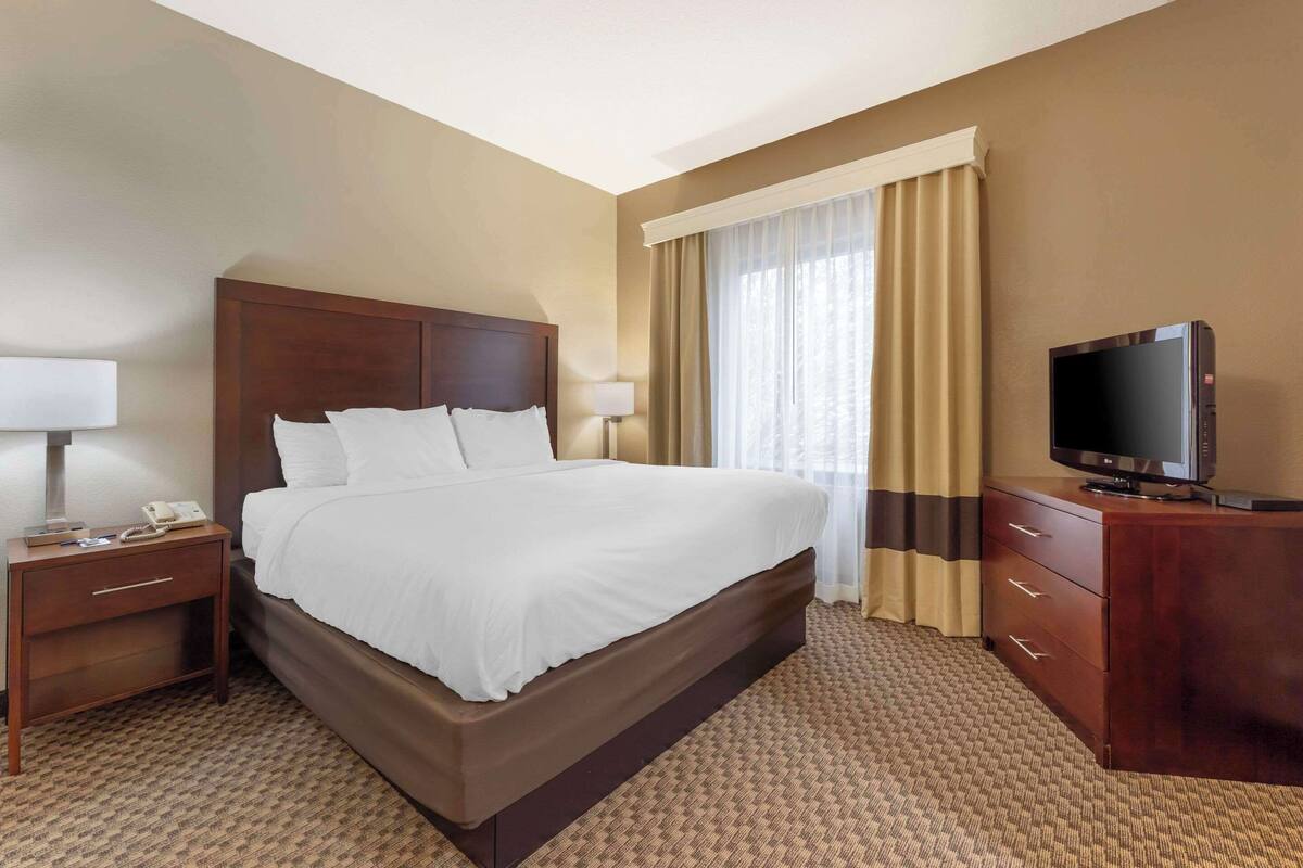Una habitación de hotel con una cama grande, un televisor, una mesita de noche y un aparador.