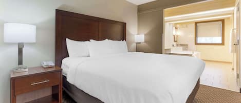 Habitación de hotel con una cama grande, una mesita de noche de madera, un escritorio y un baño visible a través de una puerta abierta.