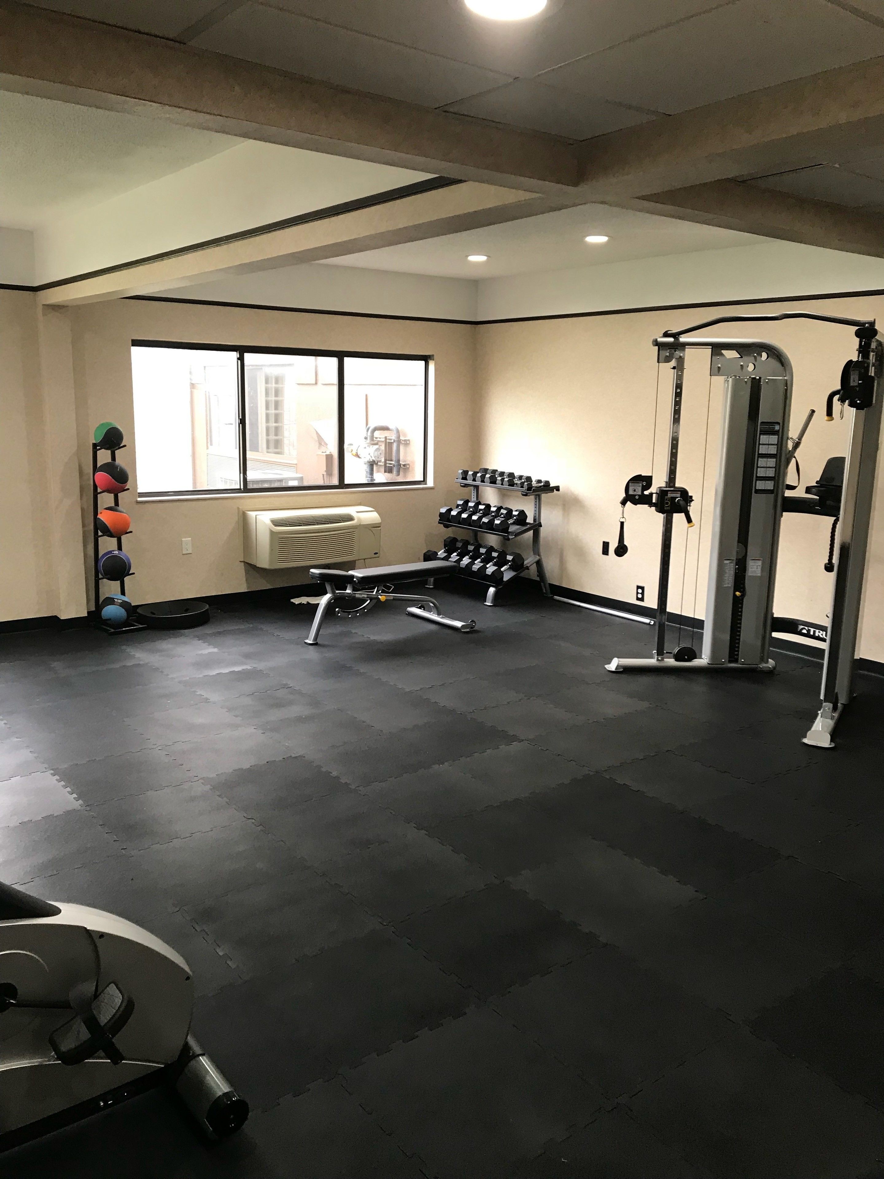Un gimnasio con equipo de ejercicio, una ventana y un aire acondicionado instalado en la pared.