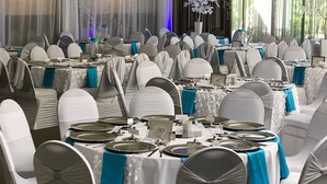 A banquet hall with round tables, white chairs, and blue tablecloths. - Days Inn & Suites by Wyndham Rochester Hills MI (Rochester)