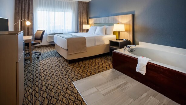 A hotel room with a bed, desk, chair, and a large bathtub. - Days Inn & Suites by Wyndham Rochester Hills MI (Rochester)