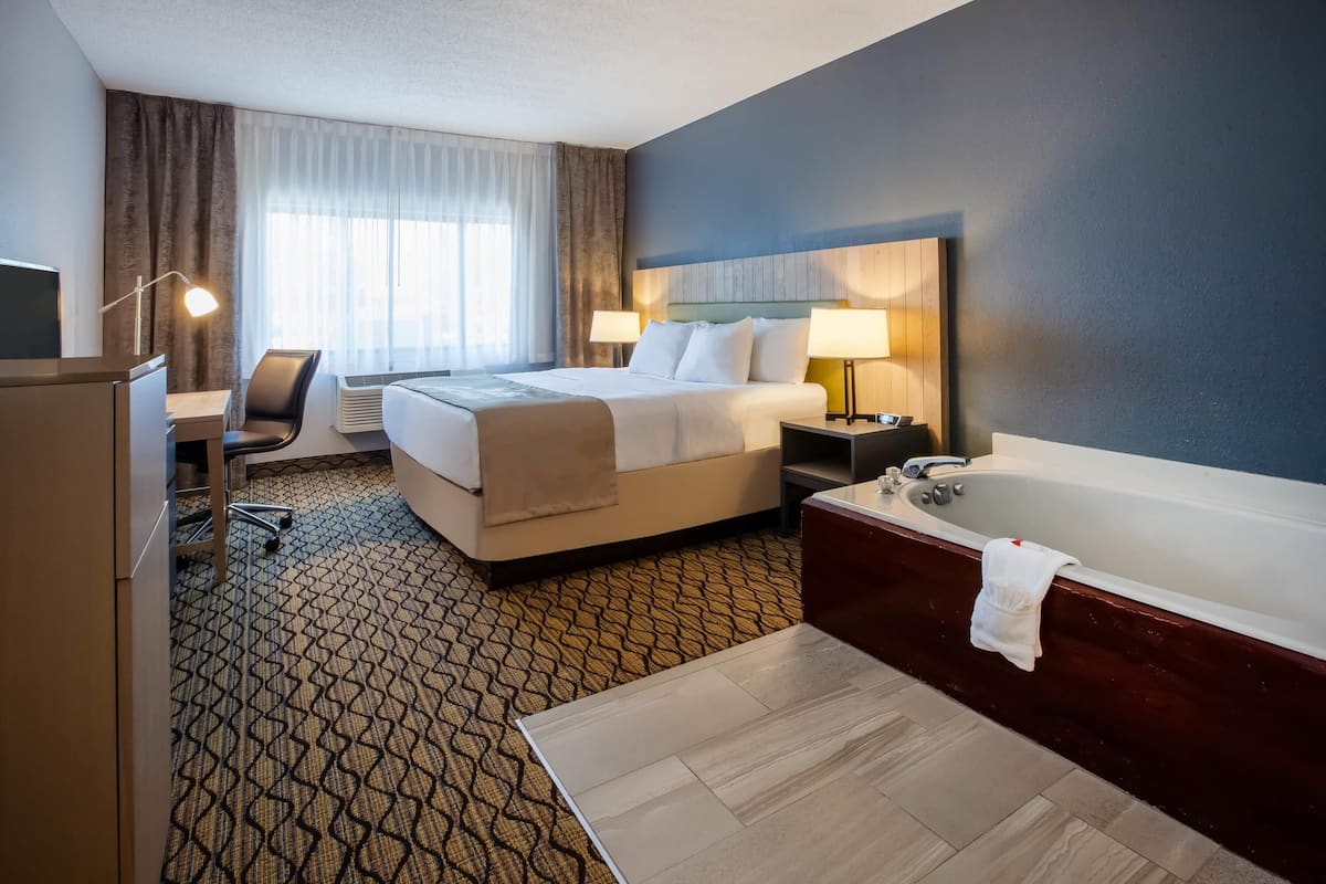 A hotel room with a bed, desk, chair, and a large bathtub.