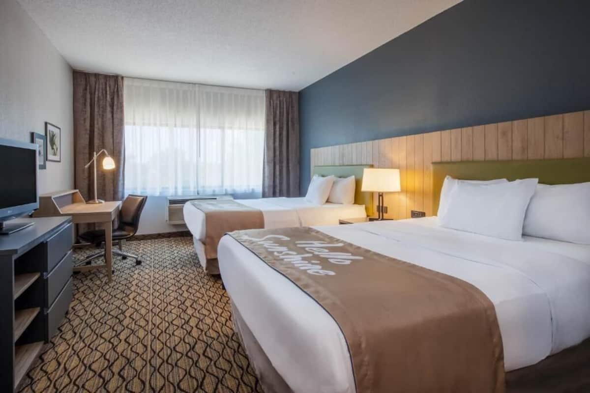 A hotel room with two beds, a desk, a chair, a TV, and a window with curtains.
