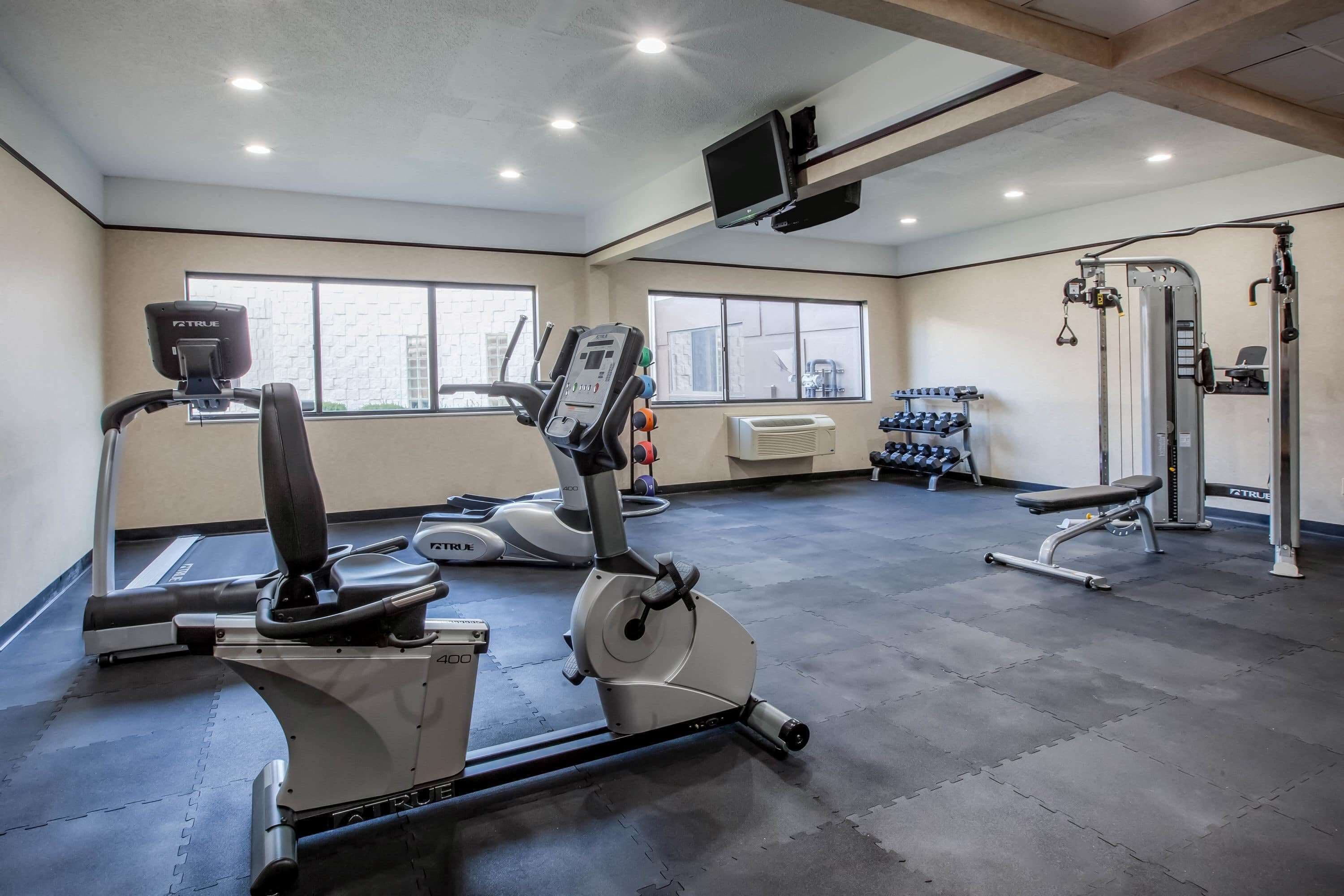 A gym with cardio machines, dumbbells, and a TV mounted on the ceiling.
